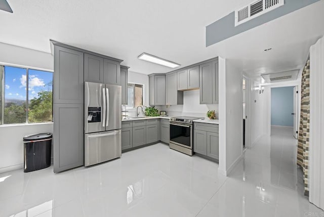 kitchen with gray cabinets, stainless steel appliances, sink, and a wealth of natural light