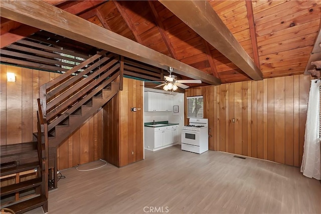 kitchen with white range with gas cooktop, wood finished floors, a sink, and wood walls