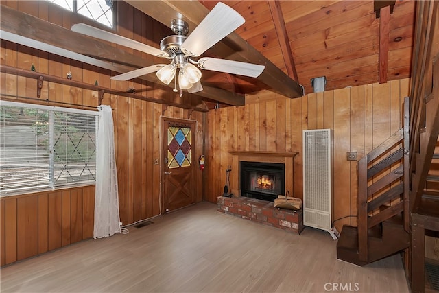 unfurnished living room with wood-type flooring, wood walls, a fireplace, vaulted ceiling with beams, and ceiling fan