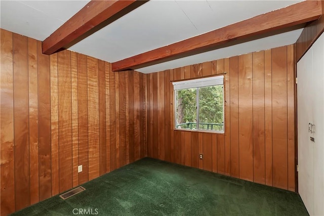 carpeted spare room featuring wood walls, beamed ceiling, and visible vents
