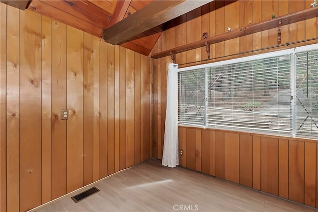 unfurnished room with wooden walls, wood finished floors, vaulted ceiling with beams, and visible vents