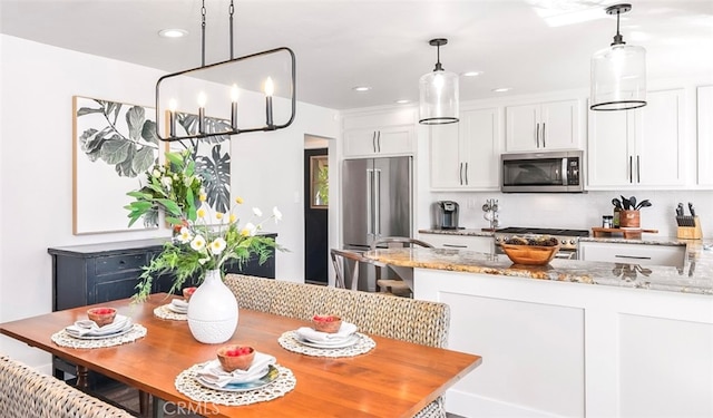 kitchen with white cabinetry, light stone countertops, pendant lighting, and stainless steel appliances