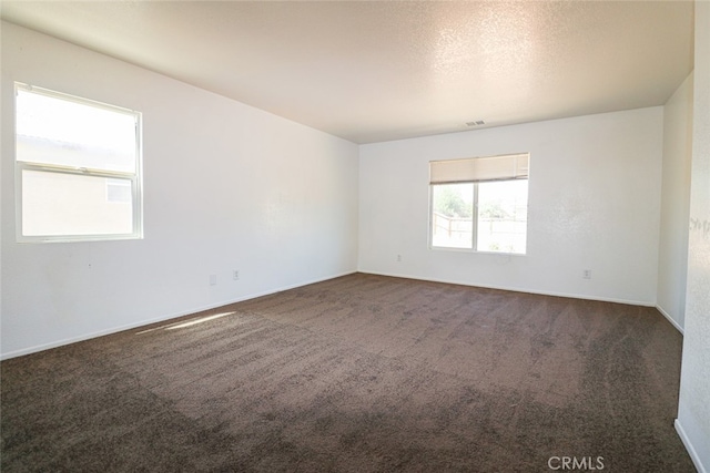 spare room featuring a textured ceiling and dark colored carpet