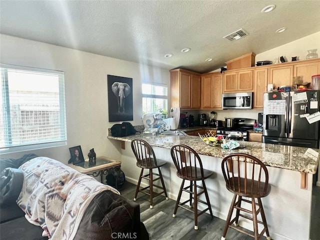 kitchen featuring a breakfast bar, kitchen peninsula, appliances with stainless steel finishes, and vaulted ceiling