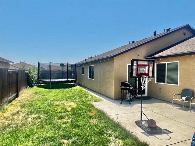 rear view of house with a patio area, a yard, and a trampoline