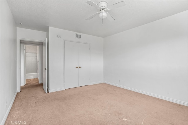 unfurnished bedroom featuring a closet, ceiling fan, a textured ceiling, and light carpet