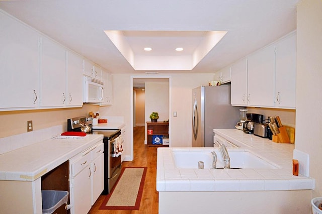 kitchen with appliances with stainless steel finishes, tile countertops, white cabinetry, and a tray ceiling