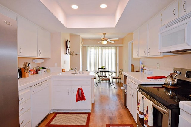 kitchen featuring a raised ceiling, light hardwood / wood-style flooring, white cabinets, and white appliances