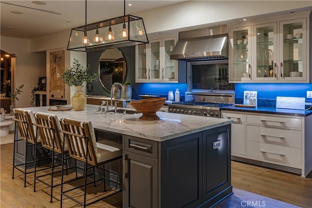 kitchen with light wood-type flooring, a center island with sink, exhaust hood, and hanging light fixtures