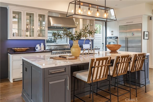 bar featuring dark stone countertops, white cabinetry, gray cabinets, range hood, and hardwood / wood-style flooring