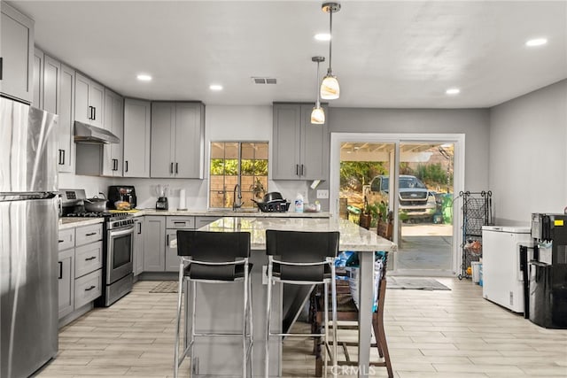 kitchen featuring a kitchen breakfast bar, stainless steel appliances, gray cabinetry, and decorative light fixtures