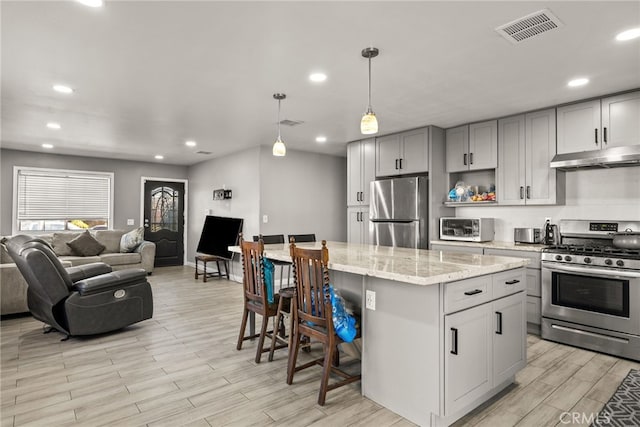 kitchen featuring appliances with stainless steel finishes, gray cabinetry, light stone counters, pendant lighting, and a center island