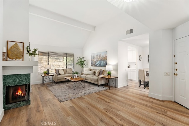 living room with beamed ceiling, a fireplace, light hardwood / wood-style floors, and high vaulted ceiling