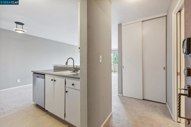 kitchen featuring vaulted ceiling, white cabinetry, sink, stainless steel dishwasher, and light colored carpet