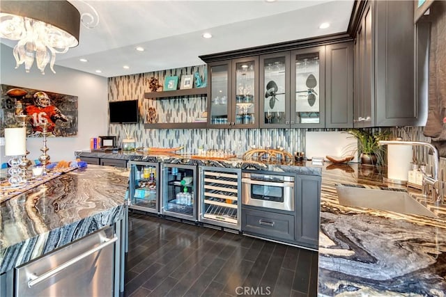 bar with dark hardwood / wood-style flooring, stainless steel appliances, beverage cooler, and sink