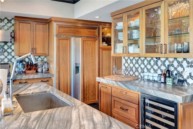 kitchen with backsplash, wine cooler, light stone countertops, and paneled built in fridge