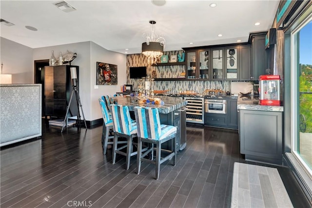 kitchen with pendant lighting, dark hardwood / wood-style floors, light stone countertops, tasteful backsplash, and beverage cooler