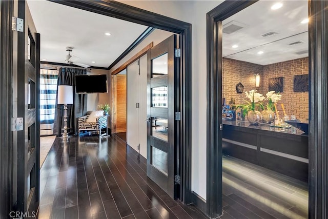 corridor with dark hardwood / wood-style floors, crown molding, and brick wall