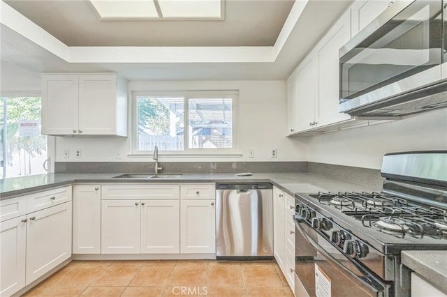 kitchen featuring appliances with stainless steel finishes, white cabinetry, a tray ceiling, light tile patterned flooring, and sink