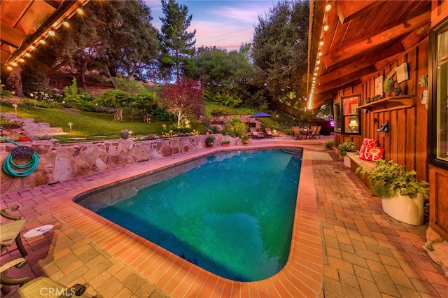 pool at dusk featuring a lawn and a patio area