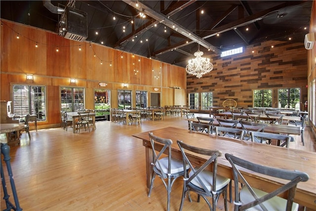 dining area featuring beam ceiling, an inviting chandelier, high vaulted ceiling, light hardwood / wood-style floors, and wood walls