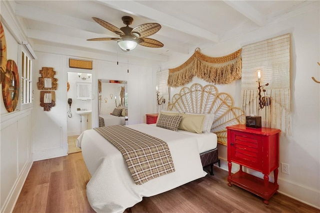 bedroom with beam ceiling, ensuite bath, ceiling fan, and wood-type flooring