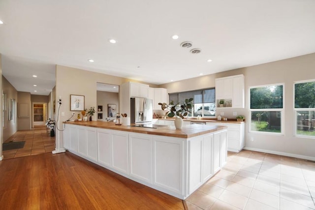 kitchen with light tile patterned floors, white cabinets, stainless steel fridge, and butcher block countertops