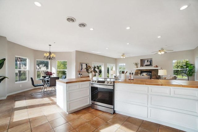 kitchen featuring stainless steel electric stove, decorative light fixtures, white cabinetry, and plenty of natural light