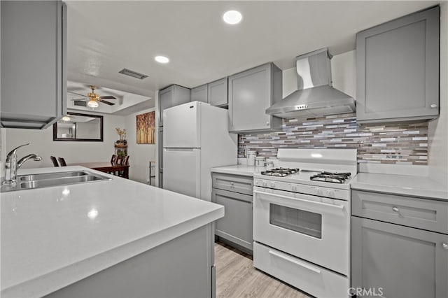 kitchen featuring light wood-type flooring, wall chimney exhaust hood, white appliances, sink, and gray cabinets