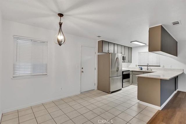 kitchen with kitchen peninsula, appliances with stainless steel finishes, light tile patterned flooring, hanging light fixtures, and sink