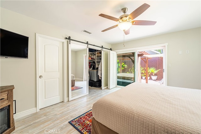 bedroom with light wood-type flooring, a closet, access to exterior, a barn door, and ceiling fan