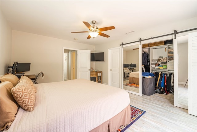 bedroom featuring a barn door, light hardwood / wood-style floors, ceiling fan, and a closet