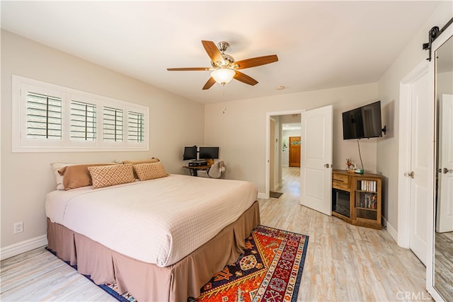 bedroom featuring light hardwood / wood-style flooring, ceiling fan, and a barn door