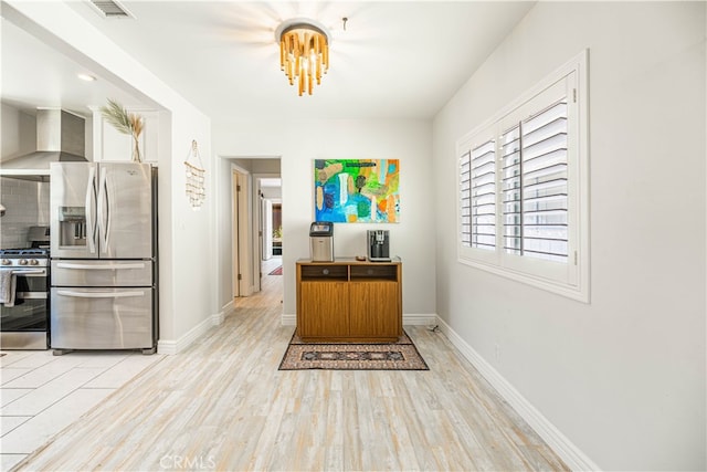 kitchen featuring backsplash, appliances with stainless steel finishes, wall chimney exhaust hood, and light hardwood / wood-style floors