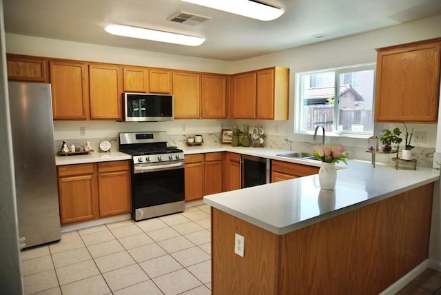 kitchen featuring sink, light tile patterned floors, kitchen peninsula, stainless steel appliances, and beverage cooler