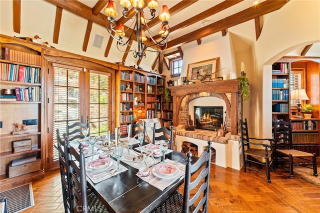 dining room with a high ceiling, beamed ceiling, a brick fireplace, a chandelier, and light parquet flooring