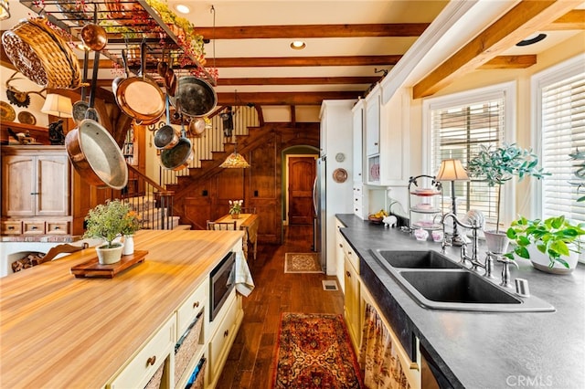 kitchen featuring butcher block counters, dark hardwood / wood-style floors, beamed ceiling, sink, and appliances with stainless steel finishes