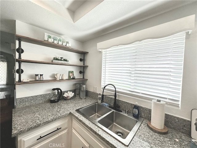 kitchen featuring white cabinetry, dark stone countertops, sink, and a textured ceiling