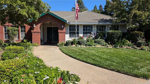 ranch-style home with a tiled roof, brick siding, and a front yard