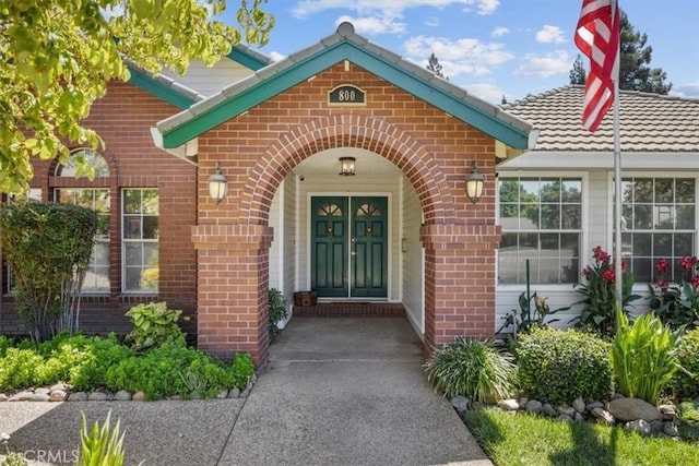 view of exterior entry with brick siding and a tile roof