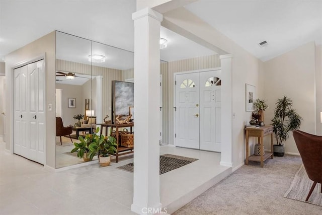 carpeted entrance foyer featuring baseboards, ceiling fan, visible vents, and decorative columns