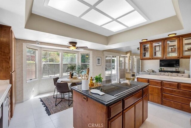 kitchen with a tray ceiling, electric cooktop, ceiling fan, and a kitchen island