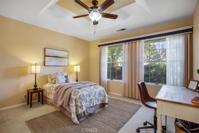 carpeted bedroom featuring a tray ceiling and ceiling fan