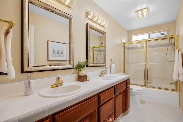 bathroom with double vanity, a sink, toilet, and bath / shower combo with glass door