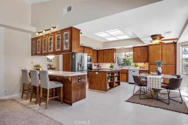 kitchen featuring visible vents, a peninsula, a kitchen bar, stainless steel appliances, and brown cabinetry