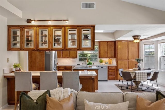 kitchen with visible vents, stainless steel appliances, glass insert cabinets, open floor plan, and brown cabinetry