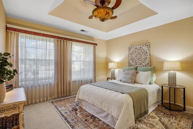 carpeted bedroom featuring a ceiling fan, a tray ceiling, baseboards, and visible vents