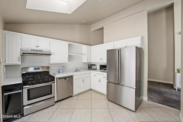 kitchen featuring backsplash, vaulted ceiling, light tile patterned floors, white cabinetry, and stainless steel appliances