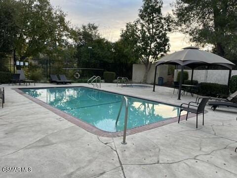 pool at dusk with a gazebo and a patio area