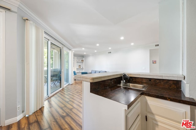 kitchen with sink, kitchen peninsula, crown molding, hardwood / wood-style floors, and white cabinets